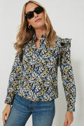 A woman stands confidently, wearing Hyacinth House sunglasses and a long-sleeve floral blouse with ruffle details, paired with blue jeans.