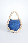The Aranaz small blue woven basket features a round opening and a handle made of large wooden beads, making it a unique handmade accessory or statement handbag.