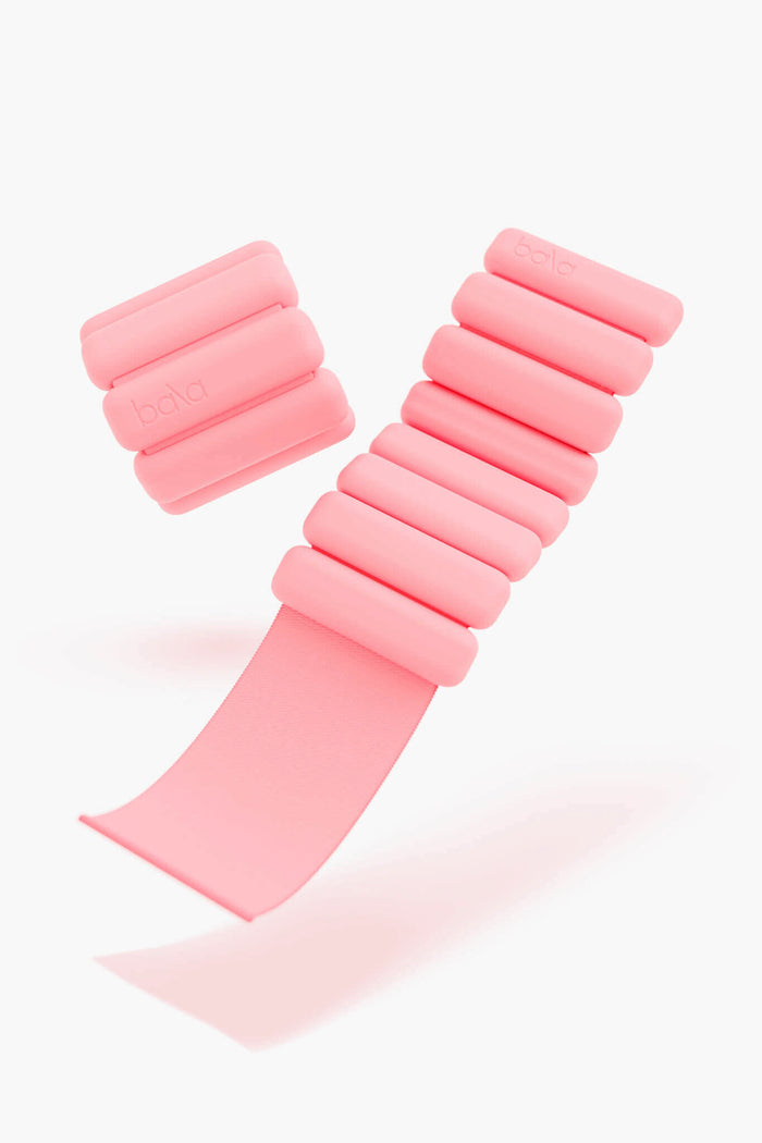 A pair of pink, adjustable Bala Bangles wearable weights from bala, made of soft silicone with cylindrical segments—ideal for adding resistance to your workout.