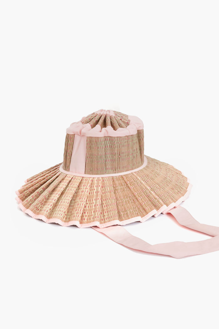 Lorna Murray’s wide-brimmed pleated straw sun hat features light pink trim, long ribbon ties, sustainable materials, and UPF 50+ sun protection.