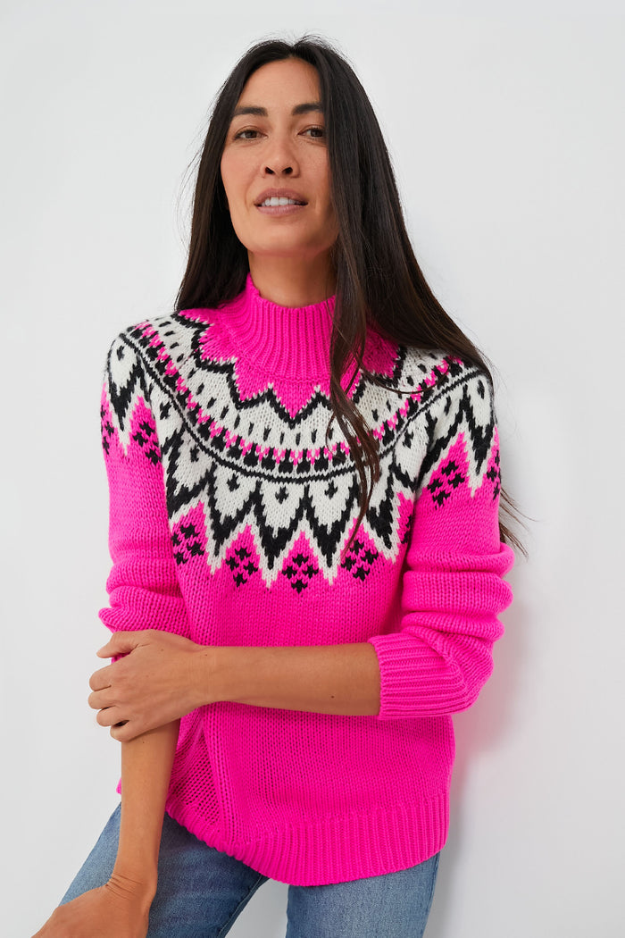 A woman with long dark hair wears the Saylor Kienna Sweater, a bright pink knit featuring a black and white Fair Isle pattern across the chest and shoulders, styled with blue jeans.