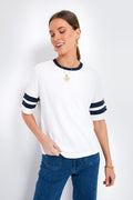 A woman wears a Faherty varsity tee made from soft pima cotton, featuring a white body with navy collar and sleeve stripes, styled with blue jeans, a gold necklace, and bracelet.