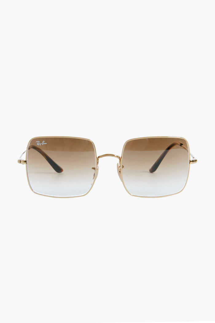 Ray-Ban rectangular sunglasses with gold frames, brown gradient lenses, and the Ray-Ban logo on the left lens, displayed in a sleek showcase.