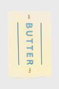 A Lynen Butter Me Up Tea Towel displays a stick of butter labeled "BUTTER" in blue, with 4 OZ and 113g in brown—an embroidered cotton kitchen towel that's perfect for your kitchen.