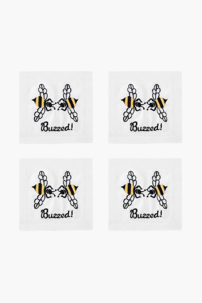 Set of four white August Morgan cocktail napkins, each with an embroidered bee above the word “Buzzed!” in black script—ideal for entertaining guests.