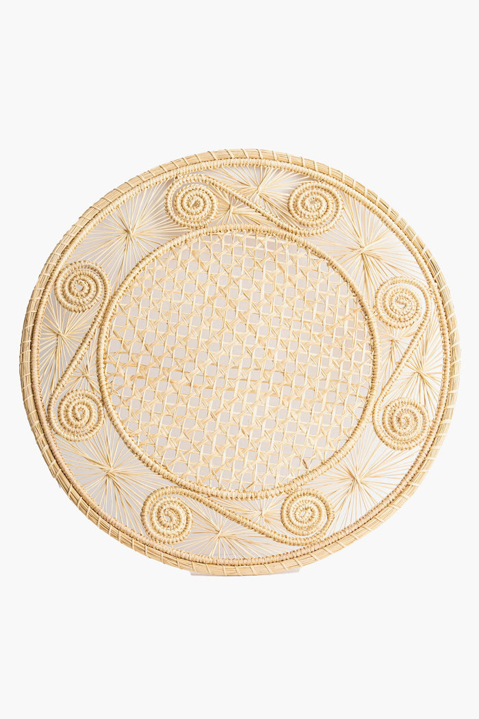 The Coro Cora round Iraca palm placemat features a woven lattice center and spiral edge designs, highlighting the beauty of Colombian handmade accessories and artisan craftsmanship.