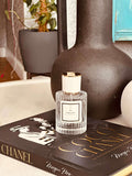 Cashmeran & Amber Eau de Parfum by LU Fragrances — 50ml glass bottle with white label and gold cap, styled on a Coco Chanel coffee table book with a large dark ceramic vase