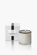 A white candle in a clear glass jar is lit beside its LAFCO New York Champagne Signature Candle box—a luxurious home fragrance and perfect housewarming gift.