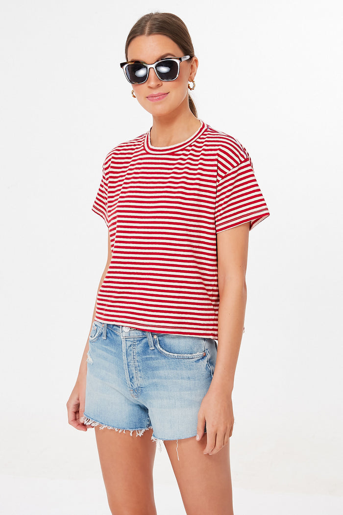 A woman stands confidently wearing black sunglasses, a candy-striped cropped tee, and light blue shorts from MOTHER.