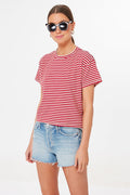 A woman stands confidently wearing black sunglasses, a candy-striped cropped tee, and light blue shorts from MOTHER.