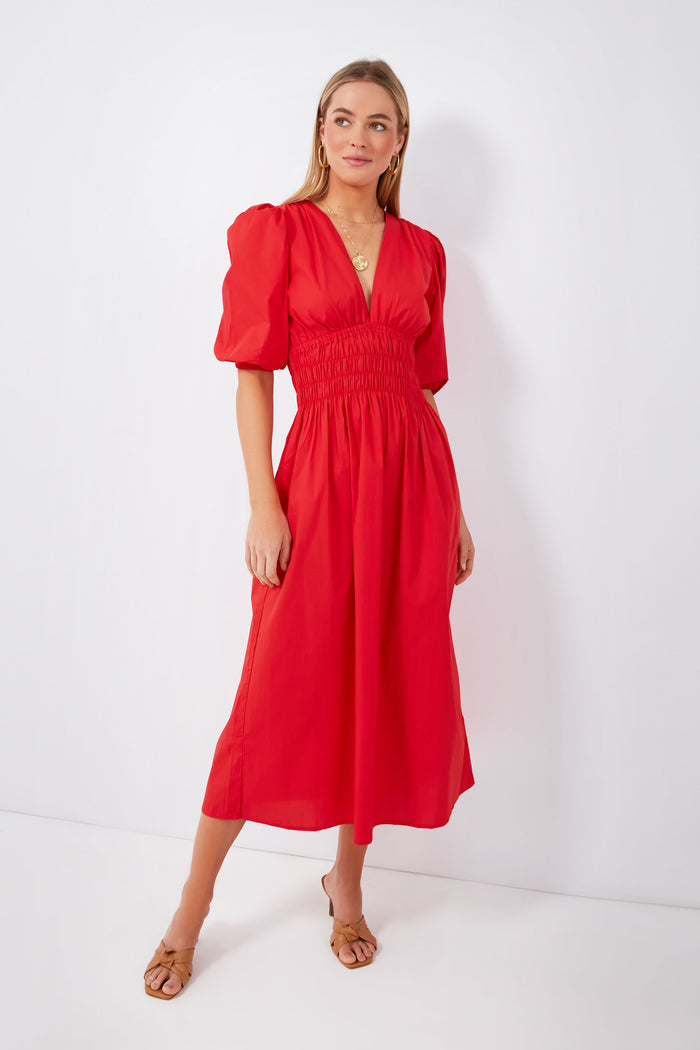 A woman wears a bright red Cherry Tomato Agnata Dress by FAITHFULL THE BRAND, an organic cotton piece with short sleeves, a shirred waist, and v-neckline, handmade in Bali.