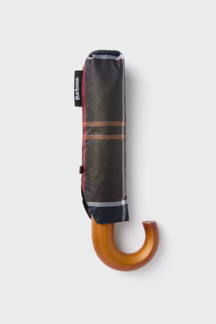 A Barbour closed umbrella with a heritage-inspired tartan pattern and curved wooden handle stands vertically.