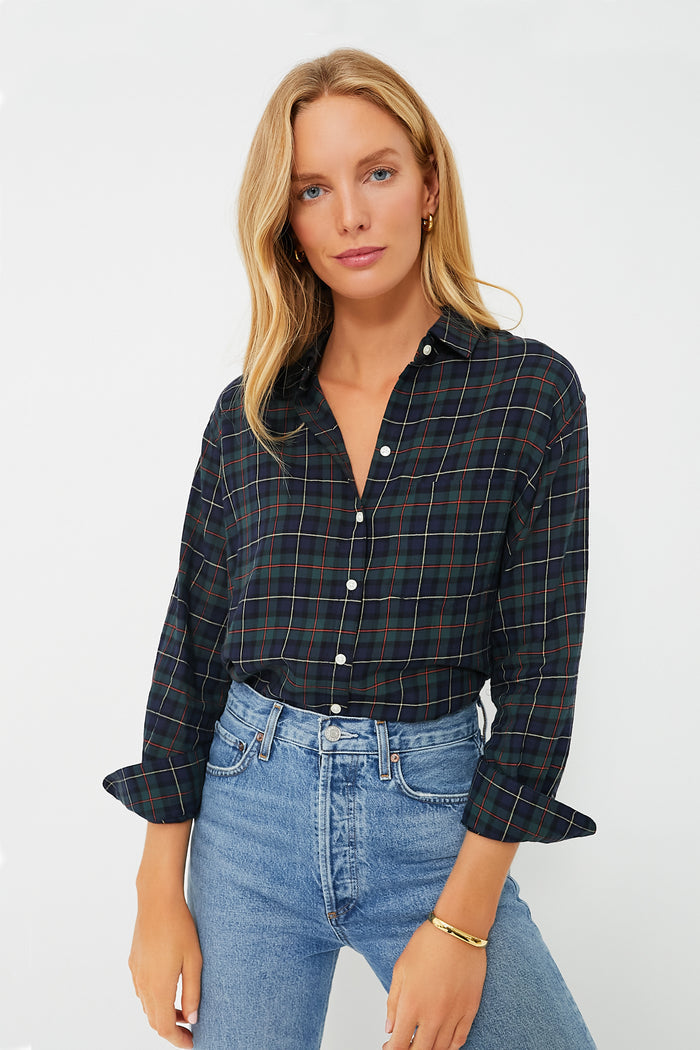 A woman with long blonde hair wears a TROVATA Birds of Paradis Plaid Blake Shirt in an oversized boyfriend fit, paired with light blue high-waisted jeans. The 100% cotton shirt features rolled sleeves for a relaxed, timeless style.