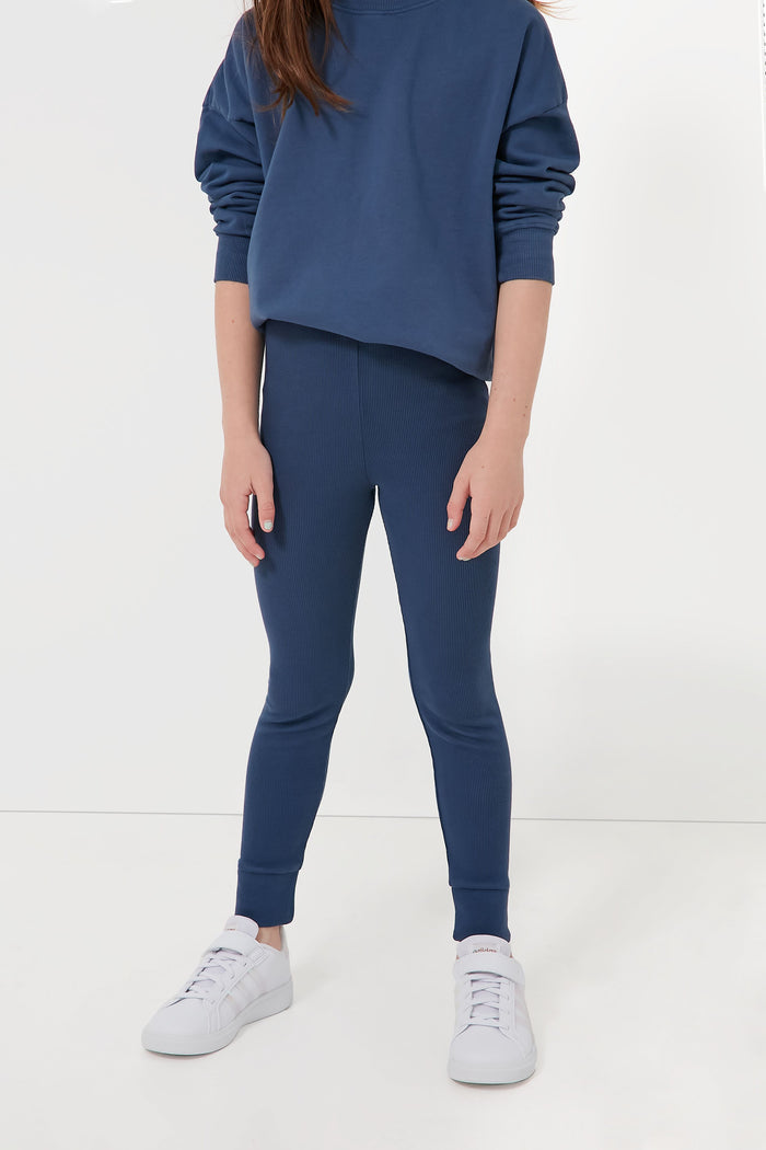 A child wears a blue Les Gamins sweatshirt, matching organic cotton leggings, and white sneakers, showcasing stylish kids’ clothing.