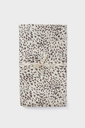 A folded cotton tablecloth with a black and white spotted pattern, tied with a cream ribbon printed with "Tuckernuck Home." Stylish and practical, this machine washable tablecloth adds charm to any setting.