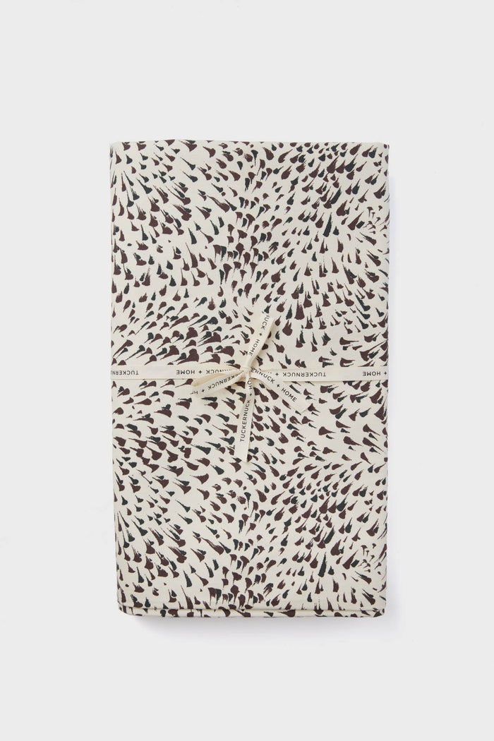 A folded cotton tablecloth with a black and white spotted pattern, tied with a cream ribbon printed with "Tuckernuck Home." Stylish and practical, this machine washable tablecloth adds charm to any setting.