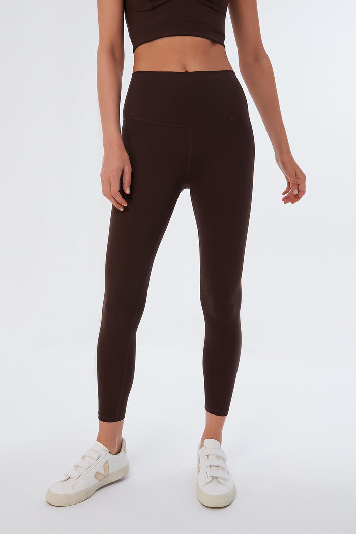 A person wears a Varley brown crop top and matching high waisted leggings with 4-way stretch, paired with white sneakers.