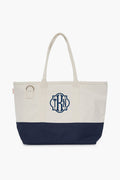 The CB Station two-tone cotton canvas bag features a cream top, navy bottom, two handles, side ring, and blue monogram on the front—an eco-friendly choice for daily use.