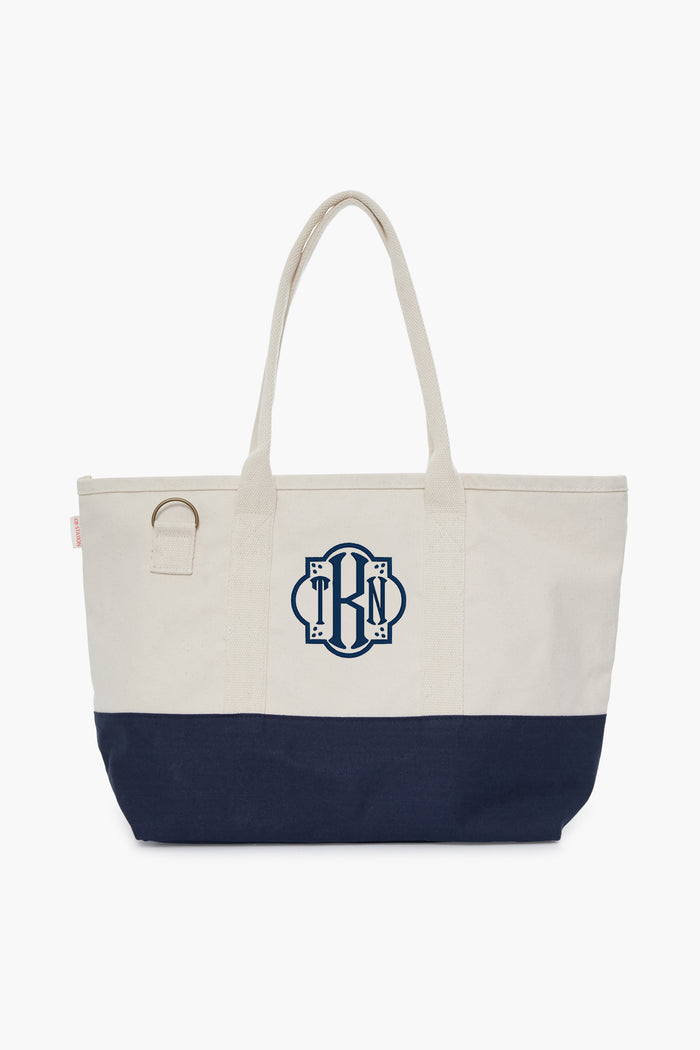 The CB Station two-tone cotton canvas bag features a cream top, navy bottom, two handles, side ring, and blue monogram on the front—an eco-friendly choice for daily use.