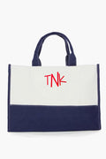 A reusable CB Station canvas tote bag with navy blue handles and bottom, a white upper section, and bold red TNK lettering—perfect for eco-conscious bag lovers.