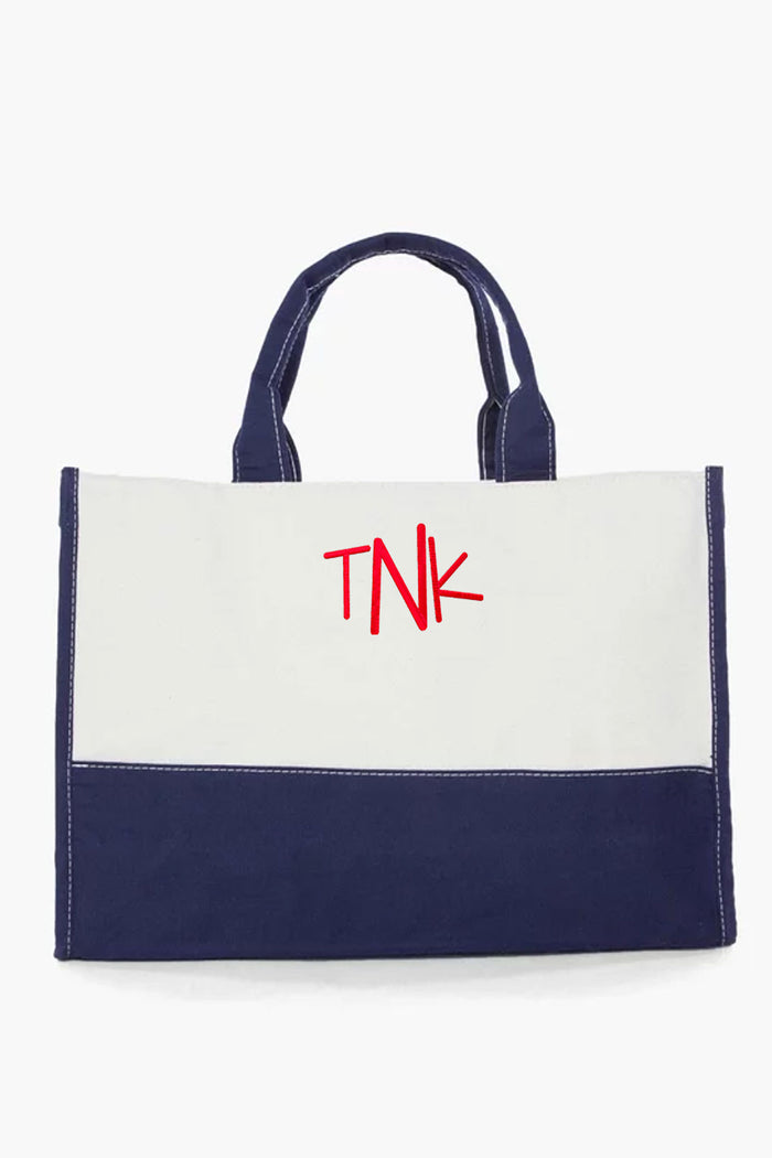 A reusable CB Station canvas tote bag with navy blue handles and bottom, a white upper section, and bold red TNK lettering—perfect for eco-conscious bag lovers.