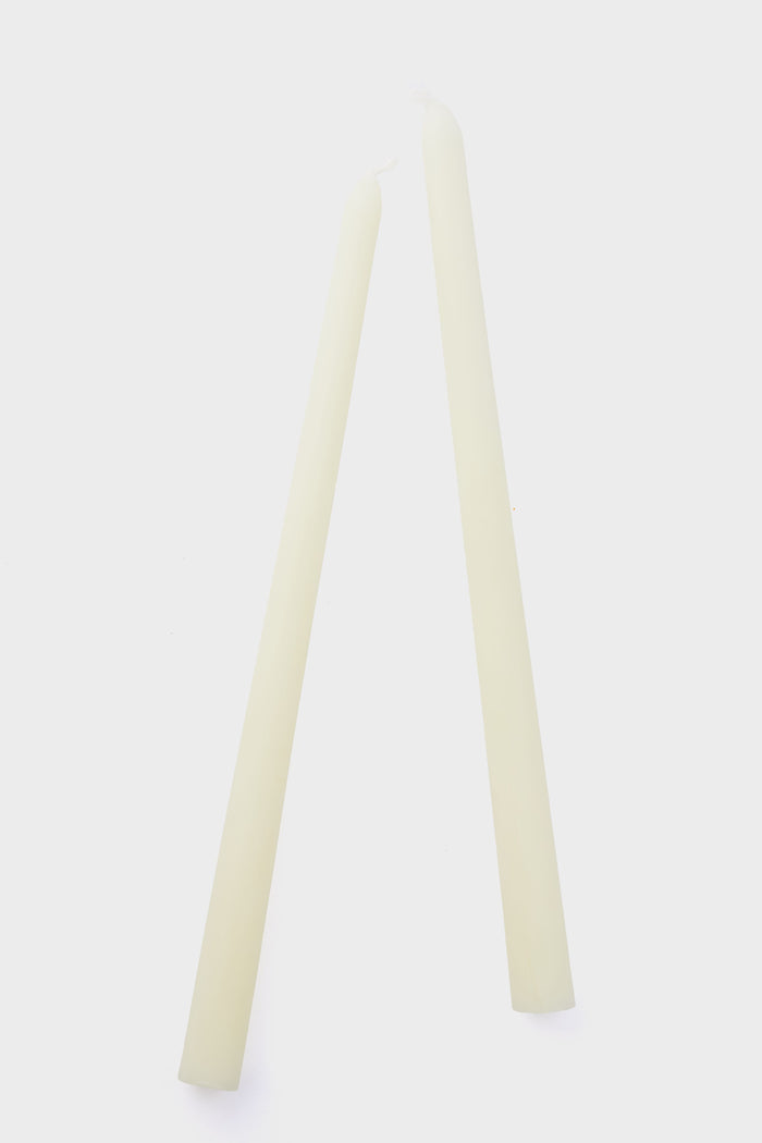 Two unlit, off-white Greentree Home handmade candles stand upright and lean together so their tips touch, showcasing the elegant simplicity of these cream tapers.