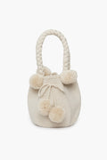A cream-colored handwoven bag by Marina Orth Foundation from San Jacinto, Colombia, featuring braided handles and decorative pom-poms.