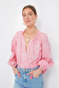 A woman wears a pink floral organic cotton blouse with oversized blouson sleeves from Love Tomas by Emerson Fry, paired with light blue jeans, gold hoop earrings, and layered necklaces for a comfortable and stylish look.