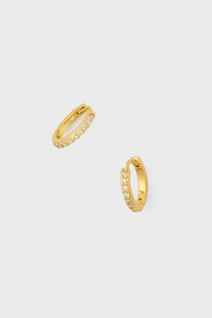 A pair of Tuckernuck Jewelry Crystal Huggie Hoop Earrings, gold plated and hypoallergenic, featuring a row of clear round gemstones set along the front.