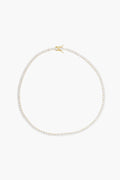 Alexa Leigh's gold tennis necklace features a single row of small, clear gemstones evenly spaced along a 14k gold fill chain, embodying contemporary jewelry style.