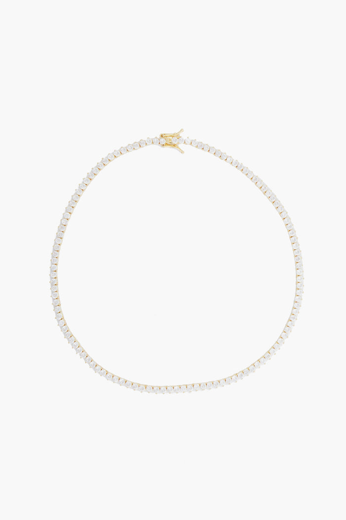 Alexa Leigh's gold tennis necklace features a single row of small, clear gemstones evenly spaced along a 14k gold fill chain, embodying contemporary jewelry style.