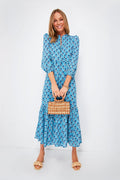 Woman in a blue floral boho dress from Love Tomas by Emerson Fry, carrying a small woven handbag and wearing beige sandals.