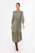 A woman wears a long green organic cotton dress with puffed sleeves, hand block printed by Love Tomas by Emerson Fry, and pairs it with brown knee-high boots.