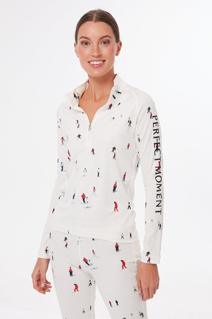 A woman wears a matching white Perfect Moment Ski Print Thermal Half Zip top and pants with small skier prints and PERFECT MOMENT text on the sleeve, ideal for après ski or chic base layering.