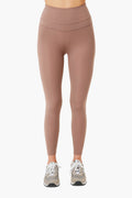 A person stands confidently wearing Varley high-waisted mauve performance leggings and gray sneakers.