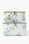 Two white rectangular Neely & Chloe x Inslee zippered toiletry bags with gold hardware and blue floral prints, stacked neatly. A chic holiday gift, these stylish bags offer elegance and smart organization for travel or your vanity.
