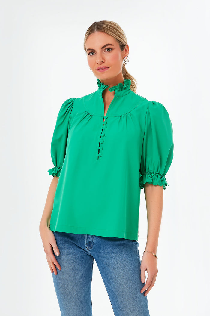 A woman wears a Pomander Place emerald green puff sleeve blouse with button details and a ruffle collar, paired with blue jeans.