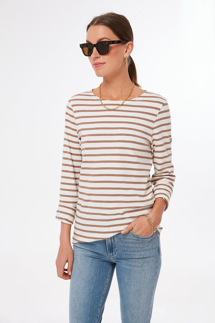 A person wearing sunglasses, Saint James sailor stripe top, blue jeans, and jewelry embodies classic French fashion.