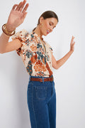 A woman smiles with her arms raised and eyes closed, wearing a Ulla Johnson feminine blouse and high-waisted blue jeans.