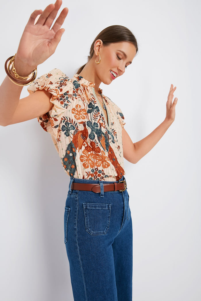 A woman smiles with her arms raised and eyes closed, wearing a Ulla Johnson feminine blouse and high-waisted blue jeans.