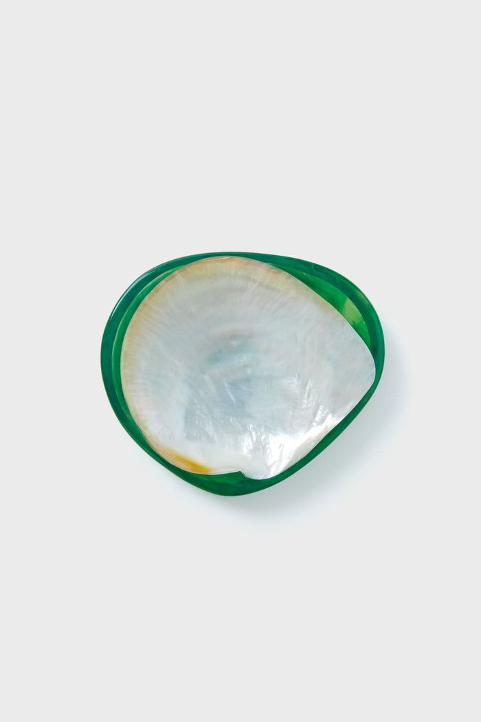 A close-up of a Lily Juliet handmade resin caviar dish shaped like a seashell, with a shiny white mother of pearl interior and green-edged exterior.