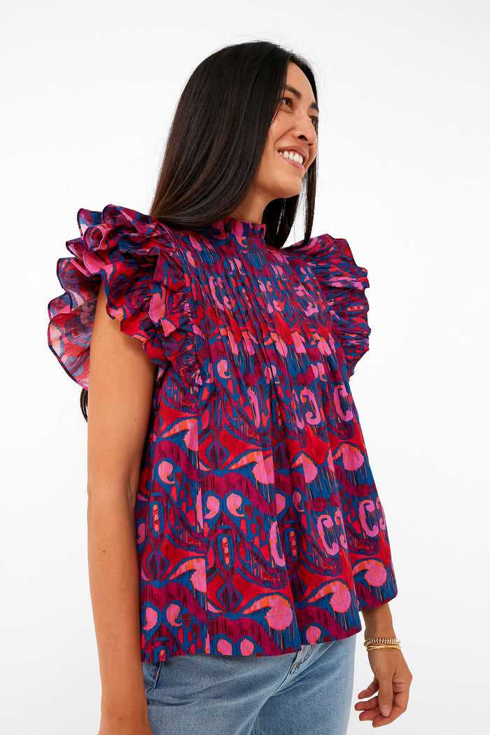 A woman stands smiling in a colorful abstract-pattern Blue Kazak Ruffle Top by Oliphant and blue jeans.