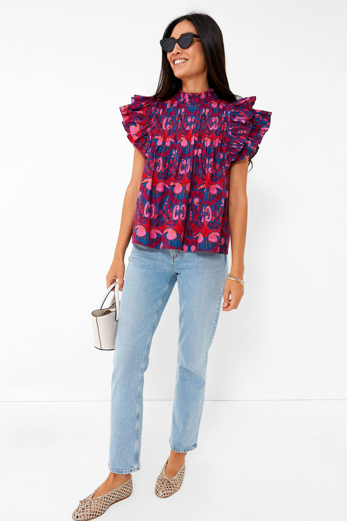 Woman models the Exclusive Blue Kazak Pintuck Ruffle Top, showcasing its classic flutter sleeves and pintucked bodice, paired effortlessly with jeans and neutral flats for a fun, high-end look.