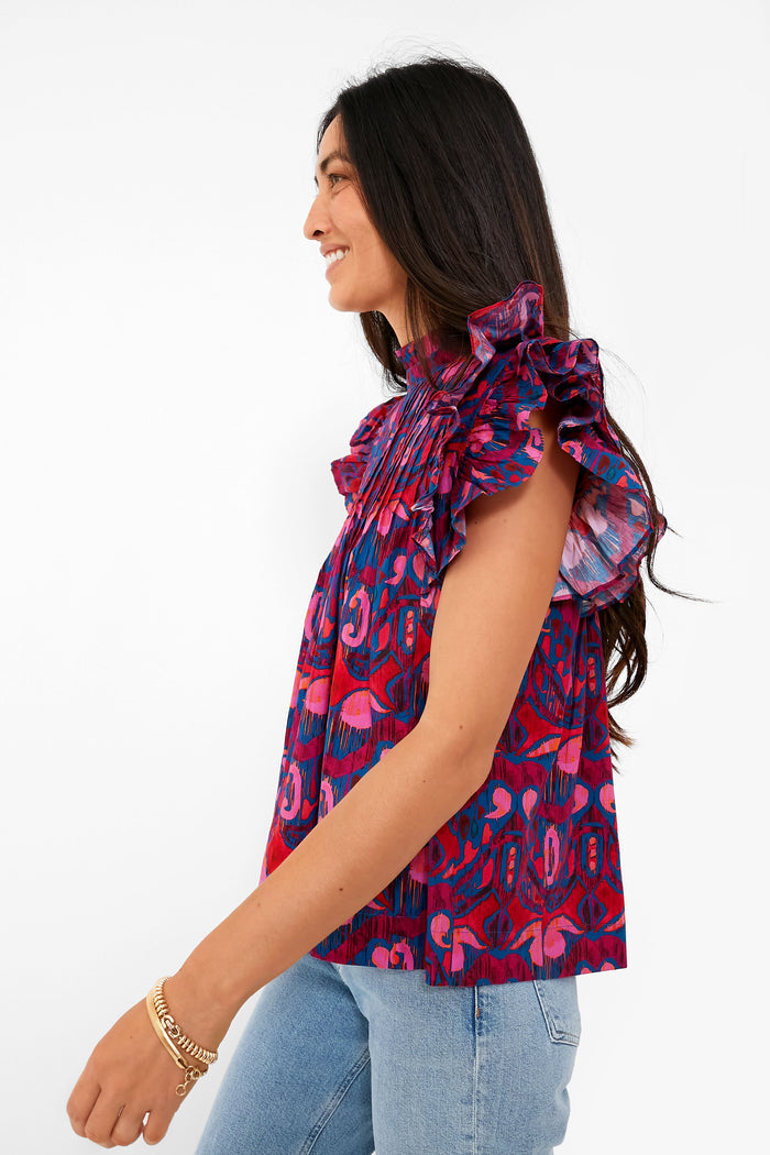 Woman in a classic, sleeveless Exclusive Blue Kazak Pintuck Ruffle Top with flutter sleeves, styled effortlessly with jeans and gold bracelets, embodying a high-end, fun fashion vibe.