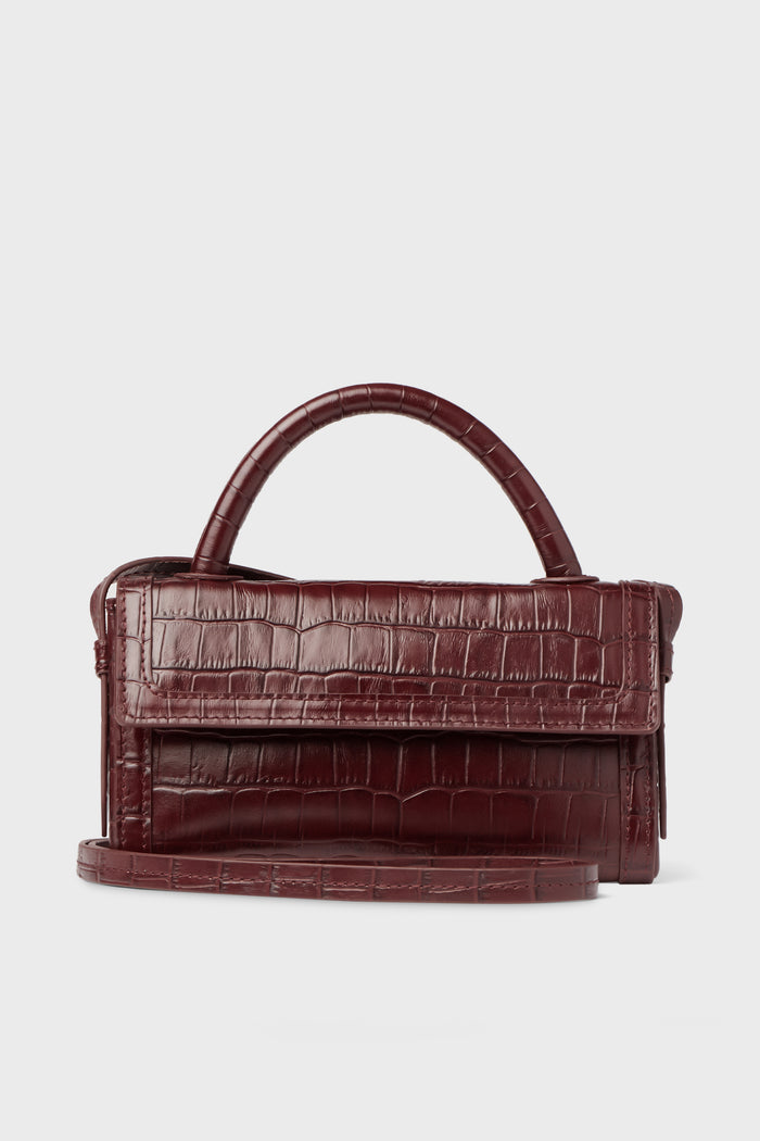 A Neely & Chloe burgundy embossed leather handbag with a crocodile texture, top handle, and long shoulder strap is displayed.