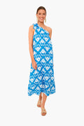 A woman wears the Nimo With Love Ikat Blue Water Lilly Dress, an elegant boho-chic one-shoulder blue-and-white midi, styled with beige sandals and drop earrings.