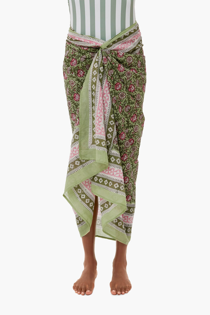 A person wears the Sunshine Tienda x Ashley Brooke Palm Sunrise Sarong tied at the waist over a green and white striped swimsuit—a barefoot, vacation-ready look ideal for pairing with beachwear accessories.