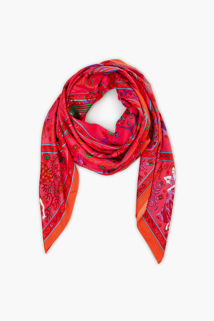 A square Vivi Designs scarf with a vibrant red and pink folklore print, showcasing floral and animal motifs, is displayed flat with ends crossed. This colorful accessory from Vivi Designs adds charm to any outfit.