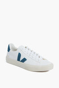 The VEJA sneaker features a white upper, blue V logo on the side, blue heel tab, white laces, and a beige eco-friendly rubber sole.