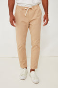 A person wears Marine Layer beige eco-friendly joggers, a white shirt, and white sneakers for a comfortable and stylish look.
